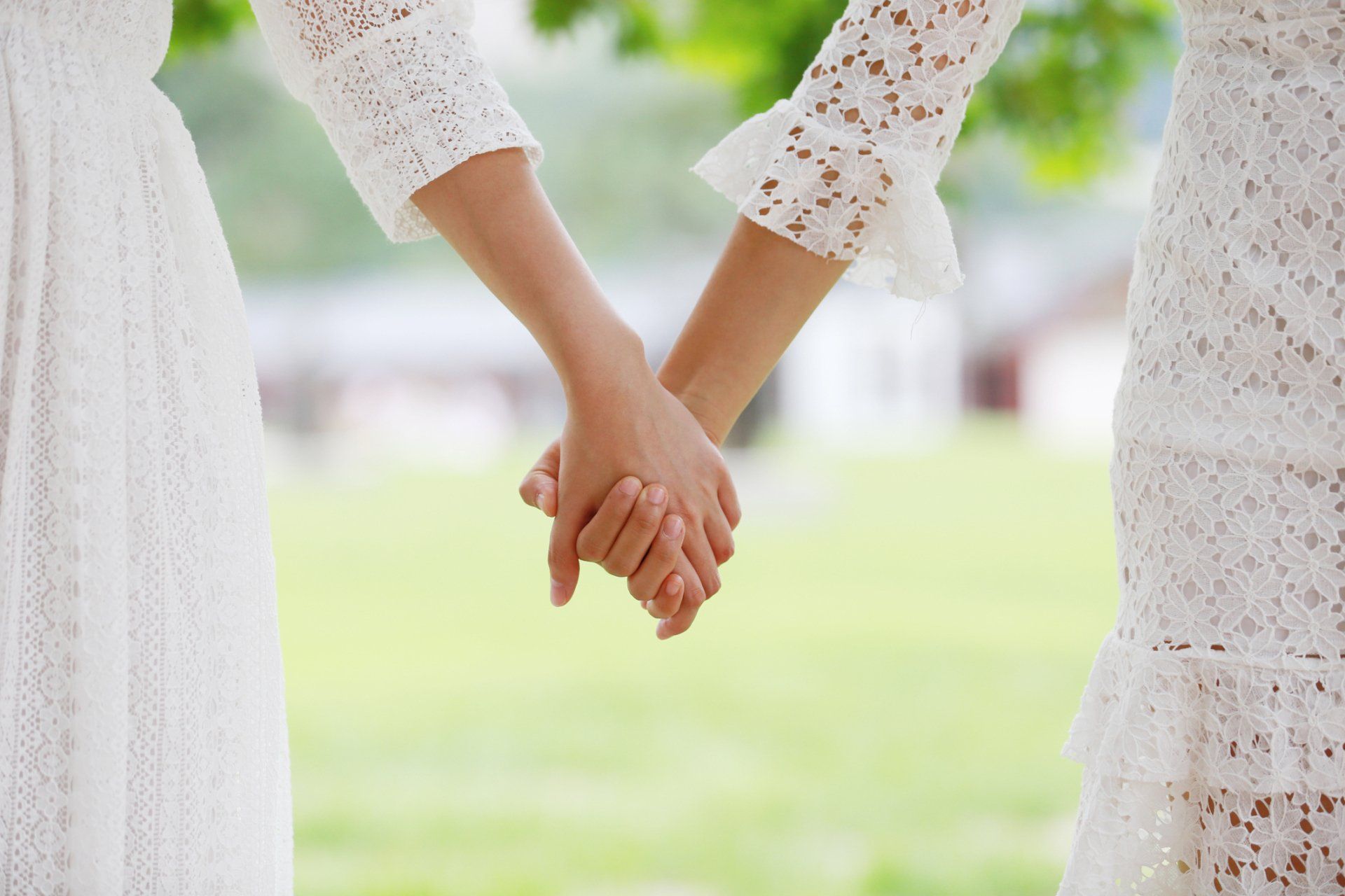 Two people in white lace dresses holding hands outdoors.